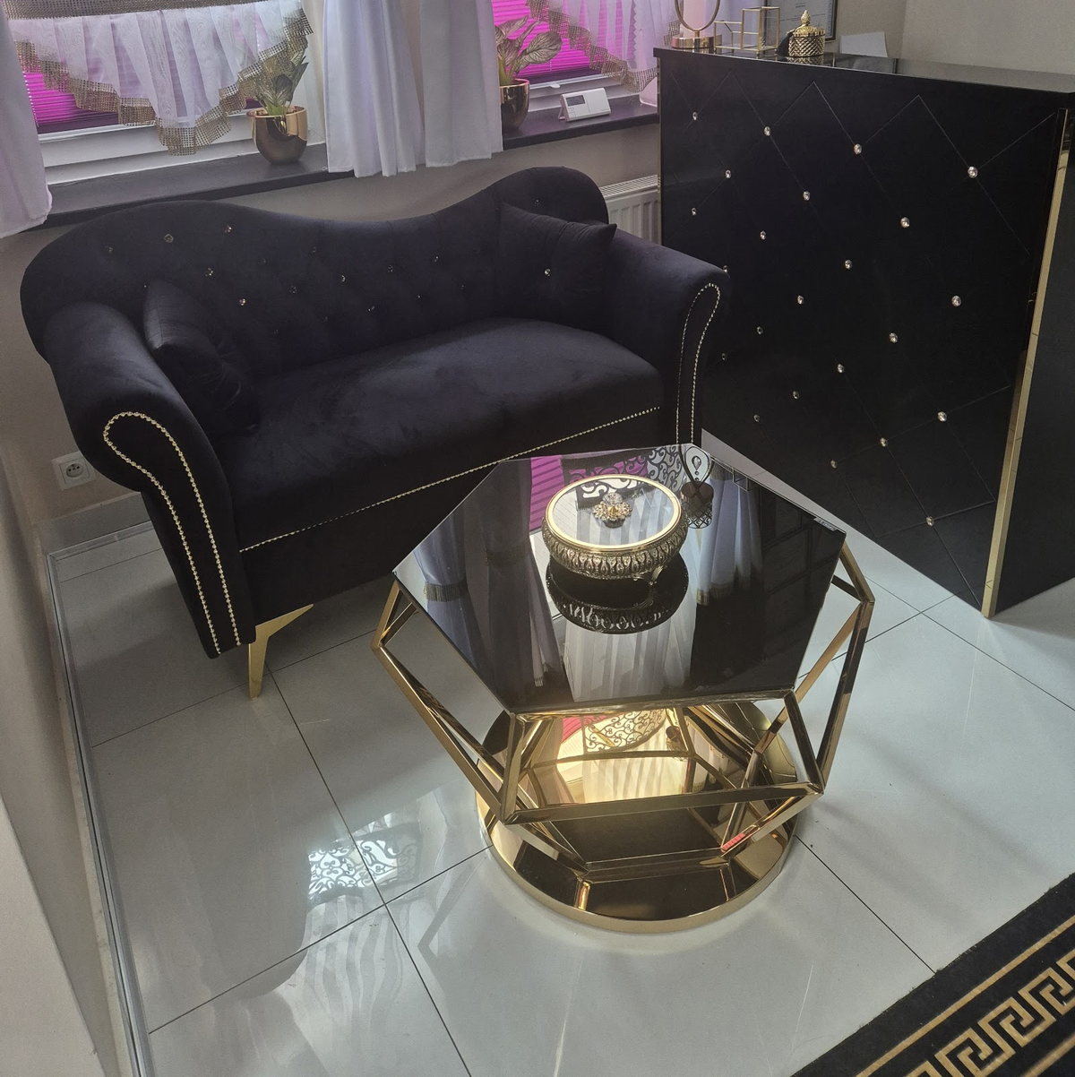 Strefa oczekiwania w małym spa Camille: czarna welurowa sofa i złoty stolik